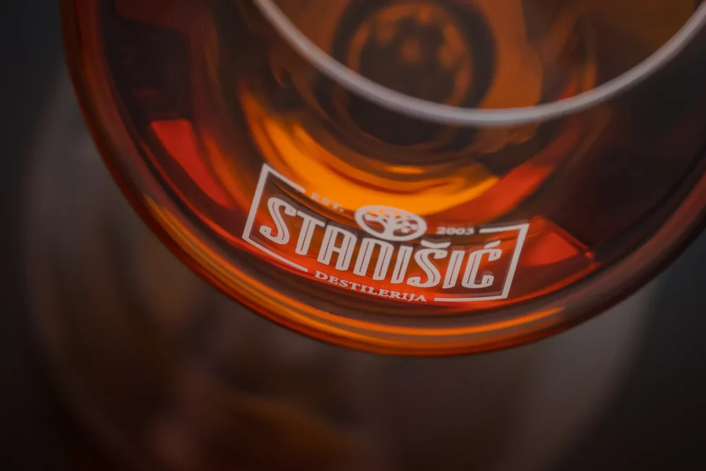 Jantarno odležano piće u čaši sa logom Destilerije Stanišić