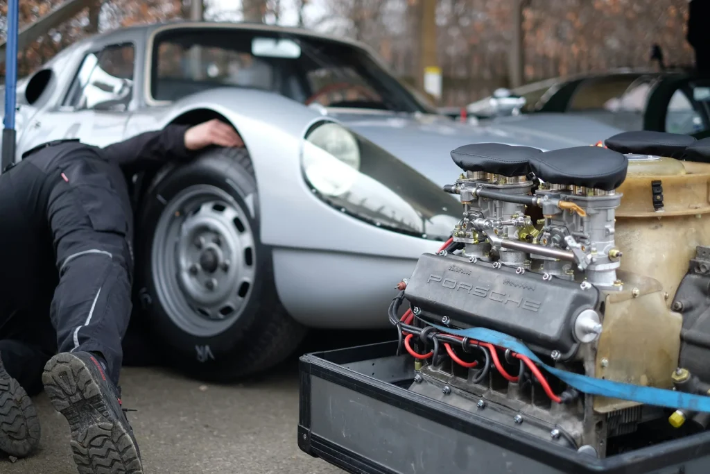 Mehaničar ispod klasičnog Porschea pored rasklopljenog motora